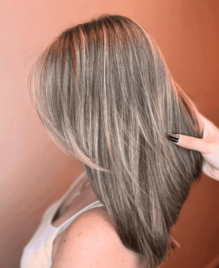 Woman with highlighted brunette hair styled in a sleek, layered cut, hand adjusting strands.
